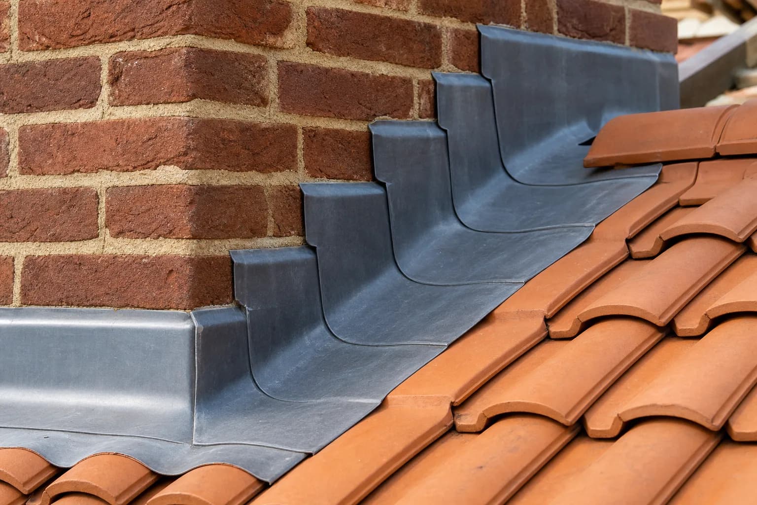 Careful roofing workmanship: lead flashing and neatly laid tiles around a brick chimney