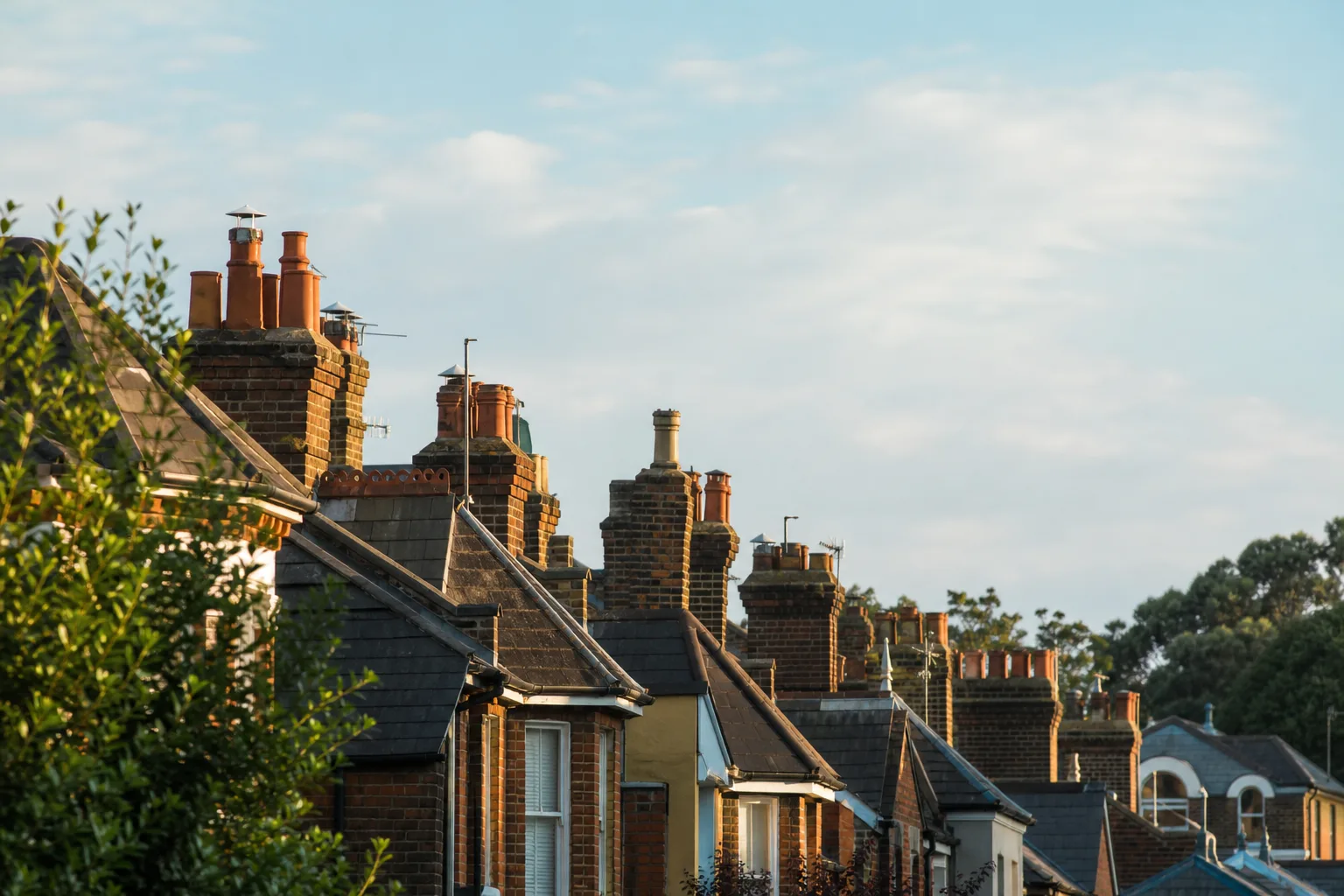 Rooftops of a quiet English residential street with chimneys under a soft blue sky