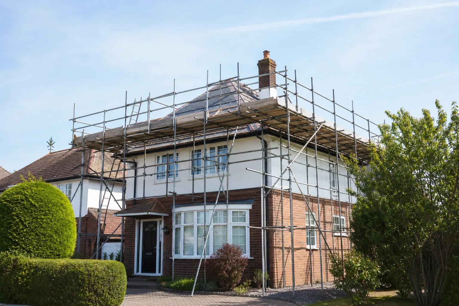 Scaffolding erected around the roof of a detached British house on a sunny day