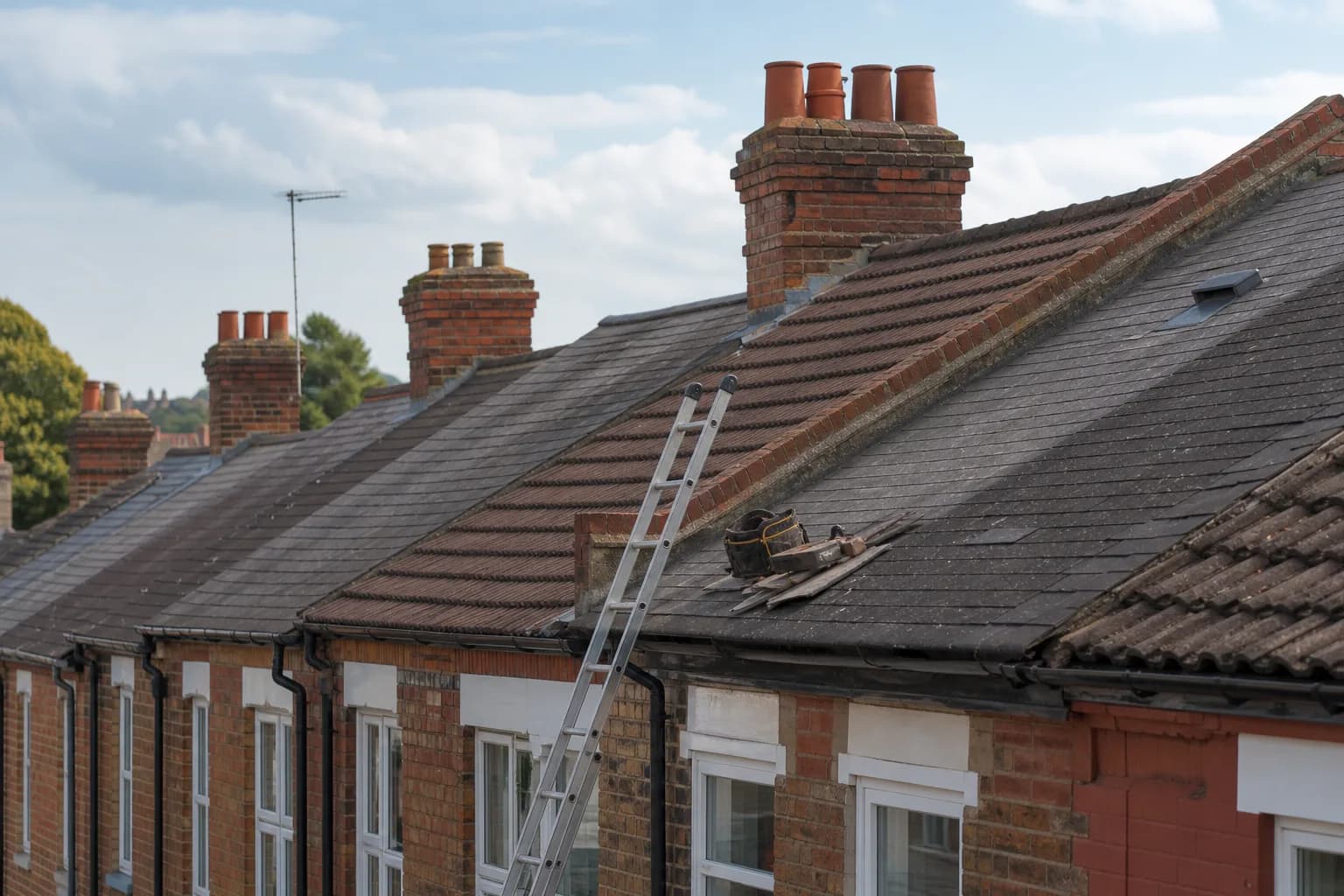 Traditional British rooftops with pitched tiles, chimney stacks and a ladder